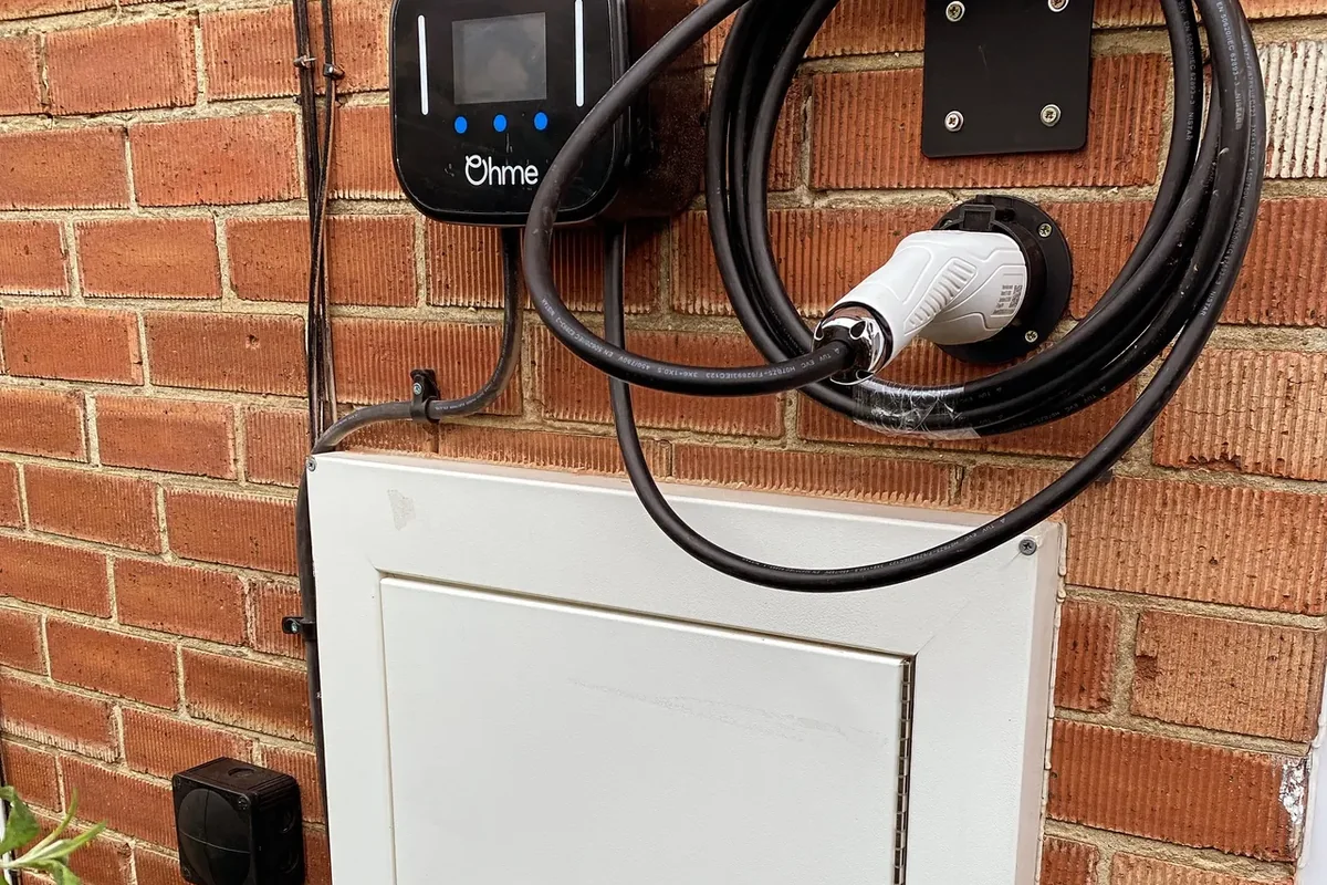 Ohme charger with coiled tethered cable on its holster beside a meter cabinet